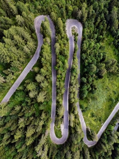 An aerial shot of a winding mountain road cutting through lush green forests