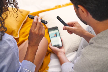 a man and woman sitting on a bed looking at a cell phone
