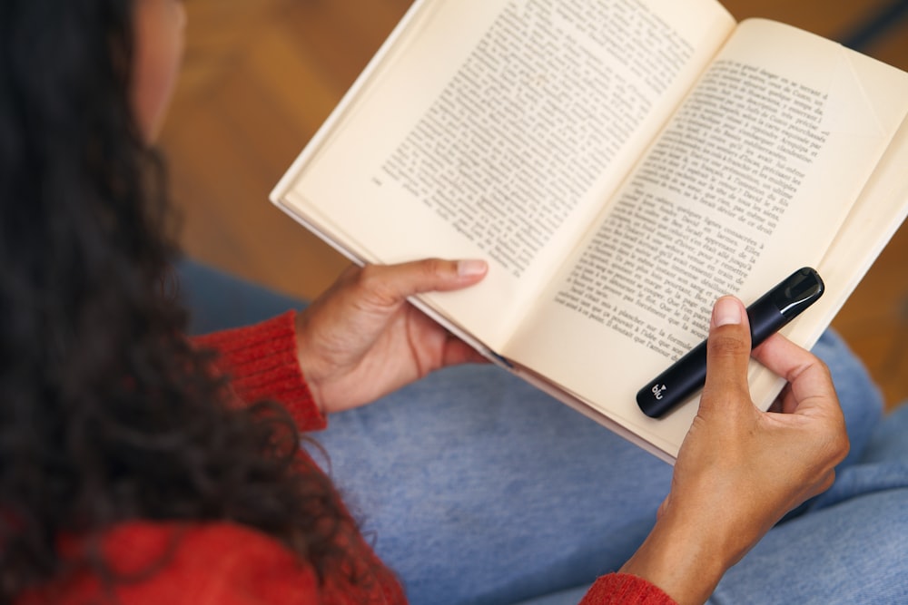 a woman is reading a book and holding a cell phone
