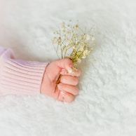 Softly lit photo of a baby's hand cast placed next to a small, delicate flower on a neutral background.