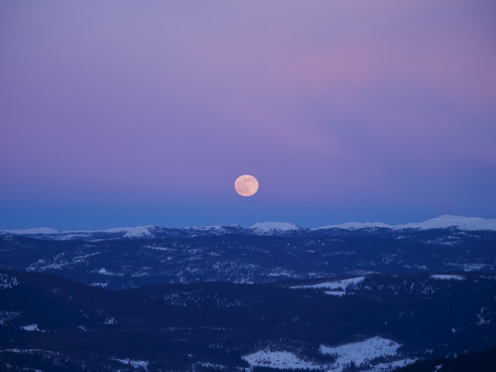 a full moon rising over a mountain range