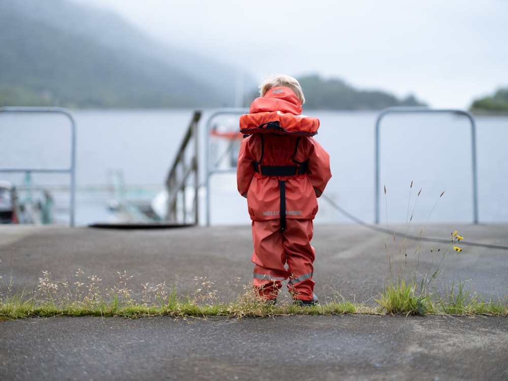 a little boy in a red rain suit looking at the water
