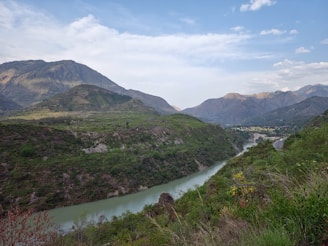 A serene landscape featuring a tranquil river surrounded by lush greenery and distant mountains.