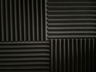 An arrangement of acoustic foam panels featuring a series of alternating vertical and horizontal ridges. The panels are positioned in a grid pattern, displaying contrasting directions of the ridges within each section. The foam texture provides a matte appearance, emphasizing the depth of the ridges.