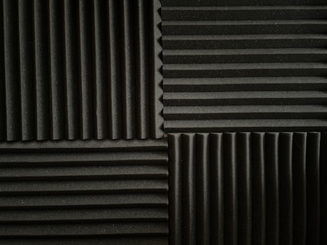 An arrangement of acoustic foam panels featuring a series of alternating vertical and horizontal ridges. The panels are positioned in a grid pattern, displaying contrasting directions of the ridges within each section. The foam texture provides a matte appearance, emphasizing the depth of the ridges.