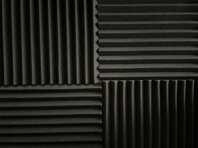 An arrangement of acoustic foam panels featuring a series of alternating vertical and horizontal ridges. The panels are positioned in a grid pattern, displaying contrasting directions of the ridges within each section. The foam texture provides a matte appearance, emphasizing the depth of the ridges.