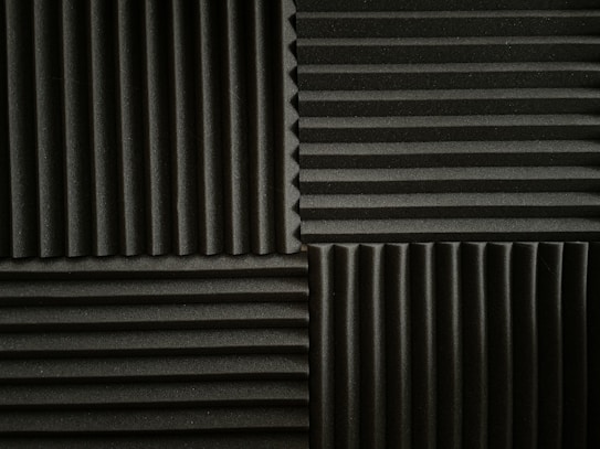 An arrangement of acoustic foam panels featuring a series of alternating vertical and horizontal ridges. The panels are positioned in a grid pattern, displaying contrasting directions of the ridges within each section. The foam texture provides a matte appearance, emphasizing the depth of the ridges.