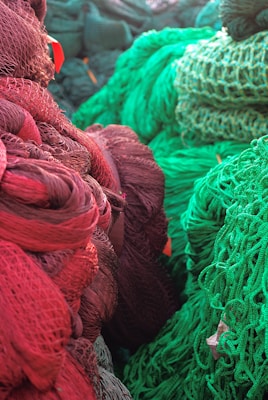 Vibrant coils of colorful fishing nets, predominantly in shades of red and green, are piled together. The texture of the nets is intricate, showcasing loops and knots, creating a rich visual tapestry.