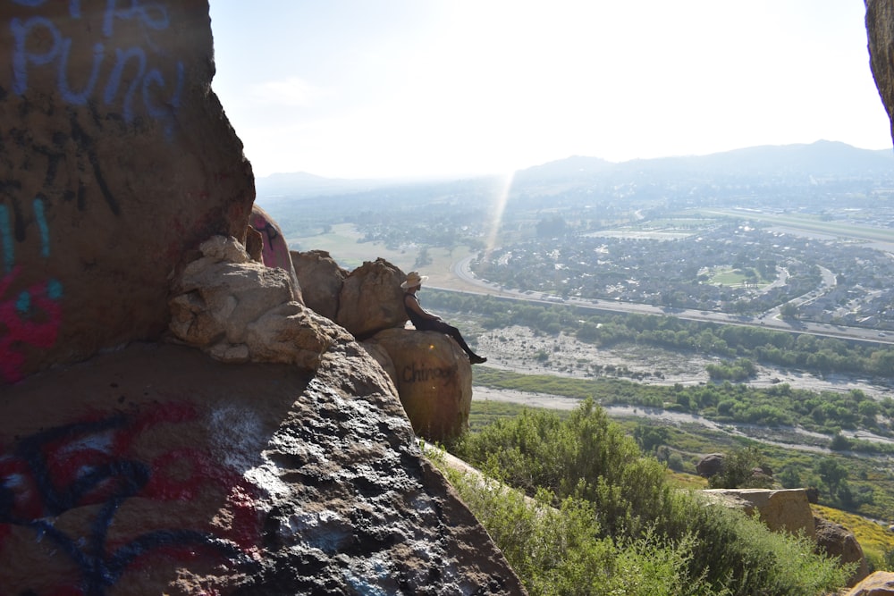 a rocky cliff with graffiti on it and a valley in the background