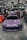 A purple Toyota sports car is prominently displayed indoors at a car show. Surrounding the car are several banners and a canopy with branding for various automotive companies. People are gathered in the background, engaging with displays and each other. The environment is well-lit with overhead lights visible on the ceiling.