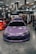 A purple Toyota sports car is prominently displayed indoors at a car show. Surrounding the car are several banners and a canopy with branding for various automotive companies. People are gathered in the background, engaging with displays and each other. The environment is well-lit with overhead lights visible on the ceiling.