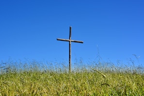 A rustic cross standing tall in a peaceful field under a bright blue sky