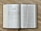 An open book displaying two pages with the title 'The Book of Tobit' on the left-hand page. The pages contain structured text in columns with headings and numbered sections. The book has a visible brown spine and rests on a wooden surface.