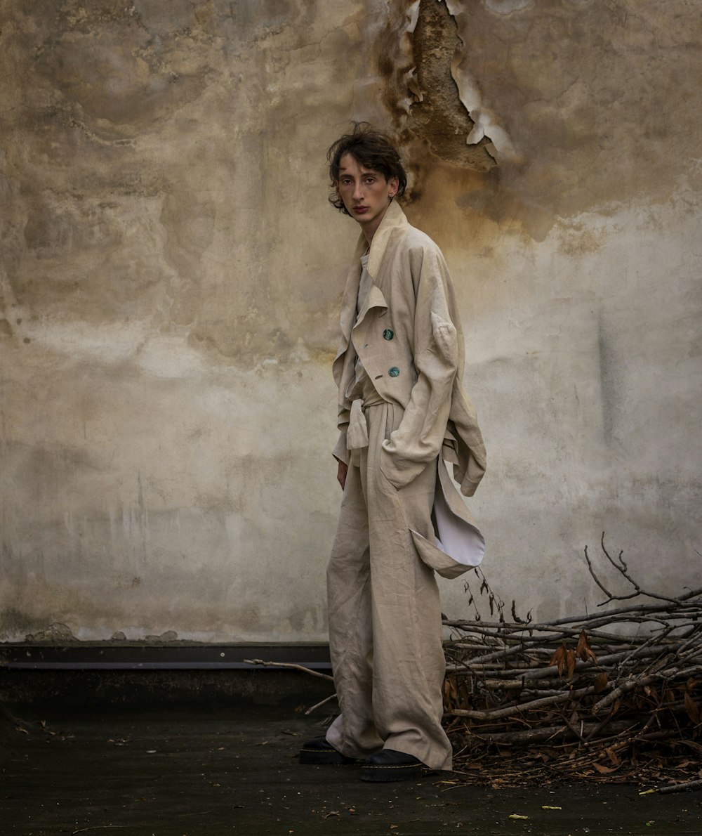 a man standing in front of a wall wearing a trench coat