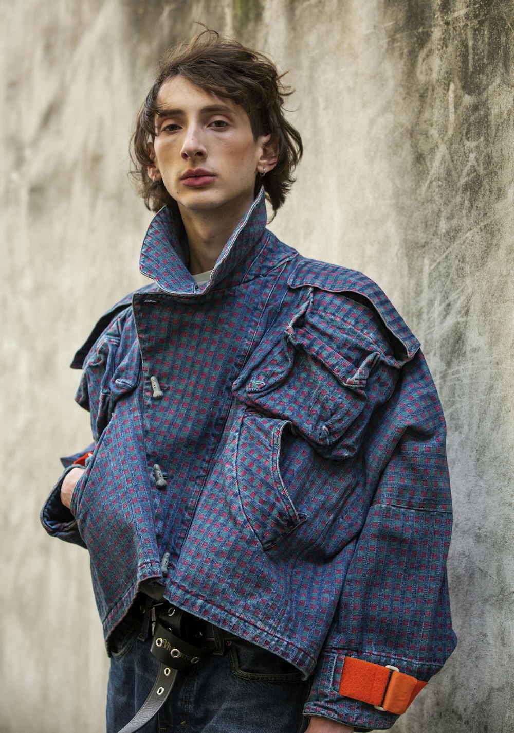 a man in a blue jacket standing next to a wall