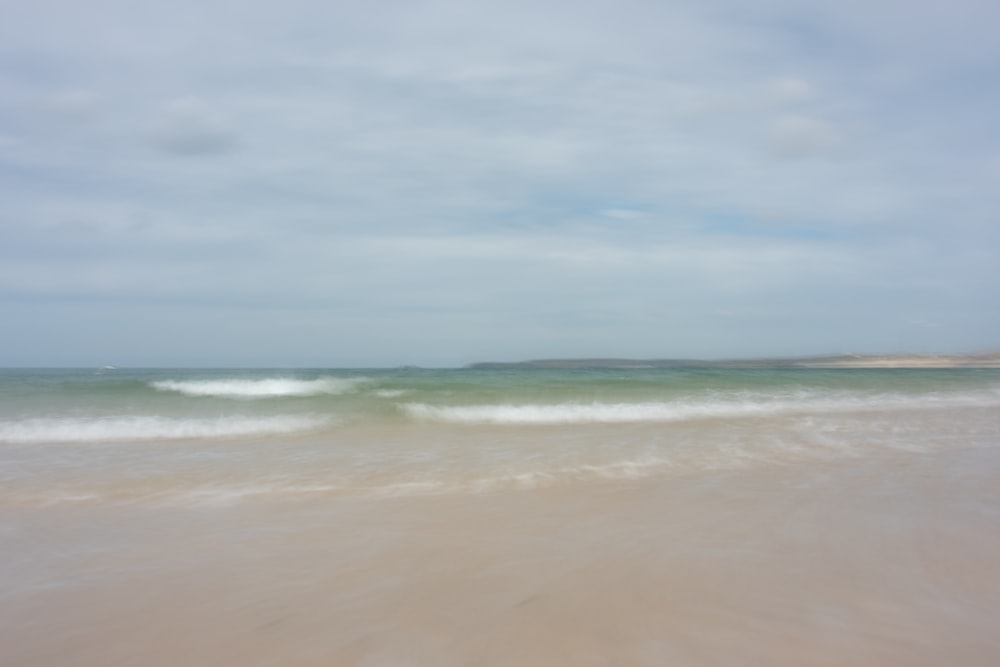 a blurry photo of a beach with a wave coming in