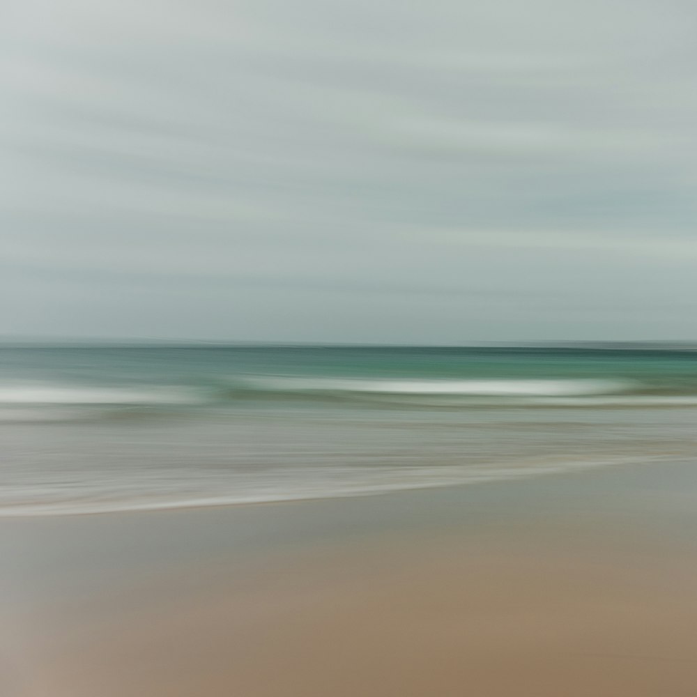 a blurry photo of a beach with a wave coming in