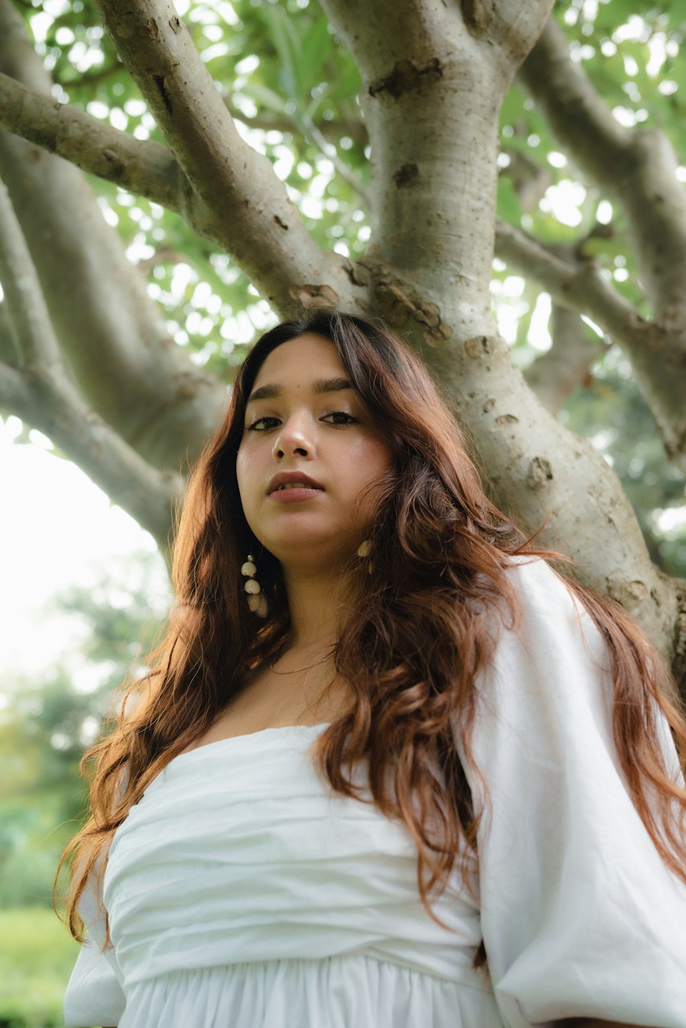 a woman in a white dress standing in front of a tree