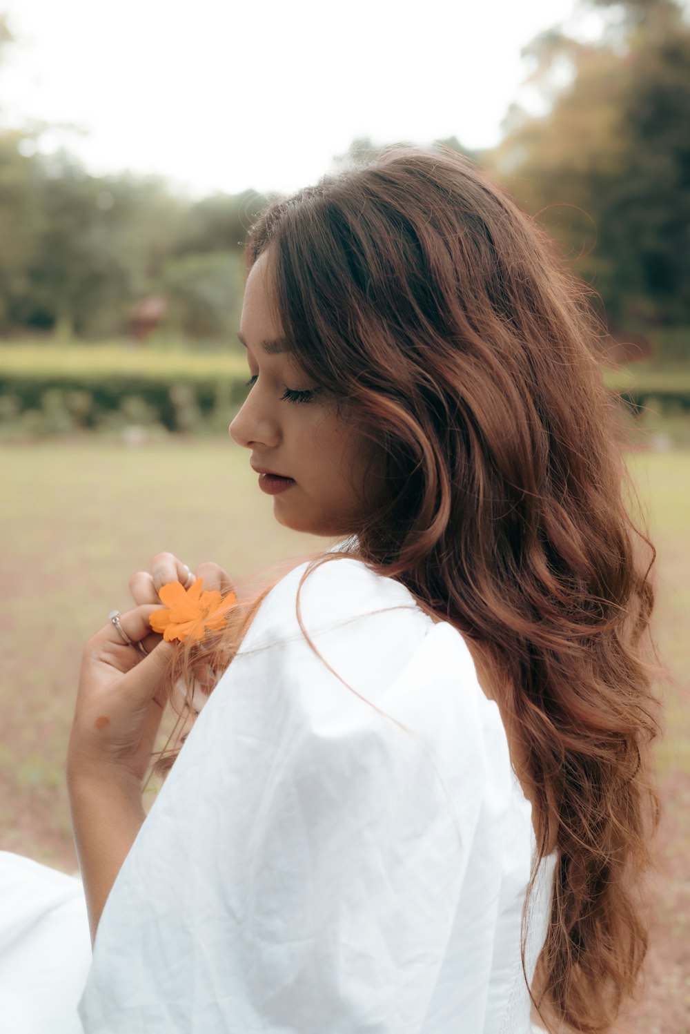 a woman in a white shirt is holding a flower