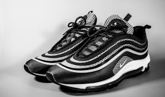A pair of stylish sneakers with a modern design featuring a black and white color scheme. The shoes have a wave-like pattern on the sides, detailed lacing, and a sleek silhouette. The background is plain, emphasizing the footwear.