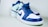 A pair of stylish sneakers featuring a blue and white color scheme. The shoes have a high-top design with blue laces and a prominent brand logo on the side panel. The background is a simple, neutral tone, highlighting the vivid colors of the sneakers.