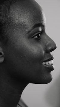 The image features a black and white profile portrait of a smiling person. The focus is on the side of the face, capturing the smooth texture of the skin and the bright expression.