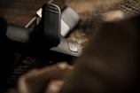 A close-up of a black USB drive with a power symbol button is placed on a textured surface. The focus on the device contrasts with the blurred foreground and background, providing an intimate and mysterious feel.
