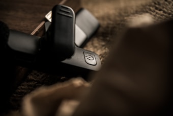 A close-up of a black USB drive with a power symbol button is placed on a textured surface. The focus on the device contrasts with the blurred foreground and background, providing an intimate and mysterious feel.