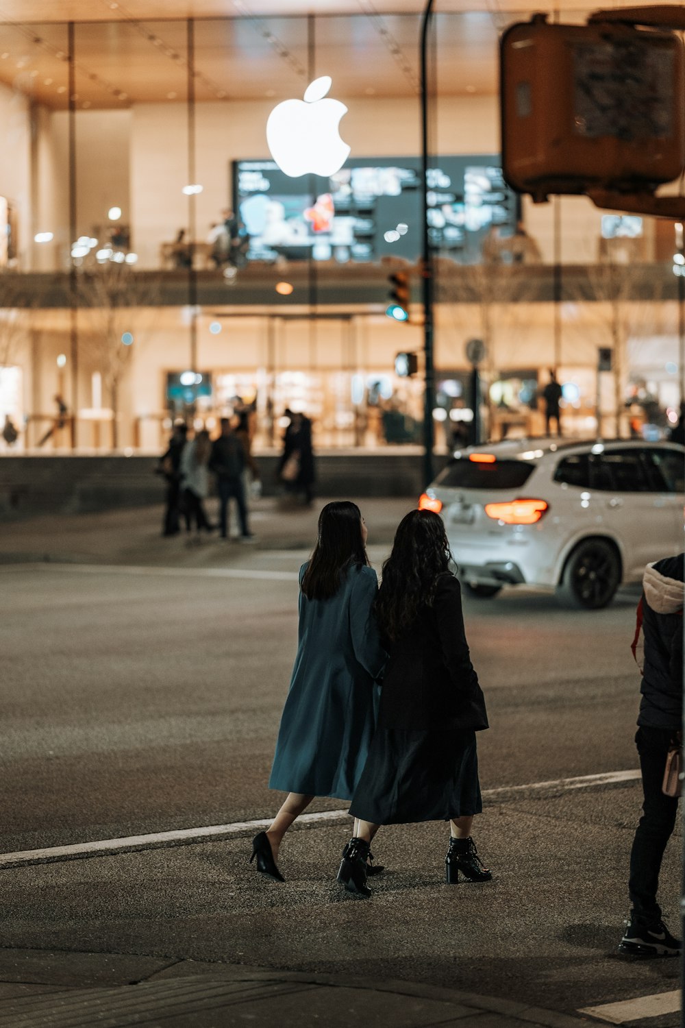 two women crossing the street in front of an apple store