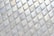 A pattern of iridescent, diamond-shaped tiles creating a textured surface with reflective qualities. The tiles are aligned in a grid with subtle color variations and swirling patterns visible on their surfaces.