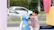 A smiling parent watching their child ride a colorful outdoor toy bike.