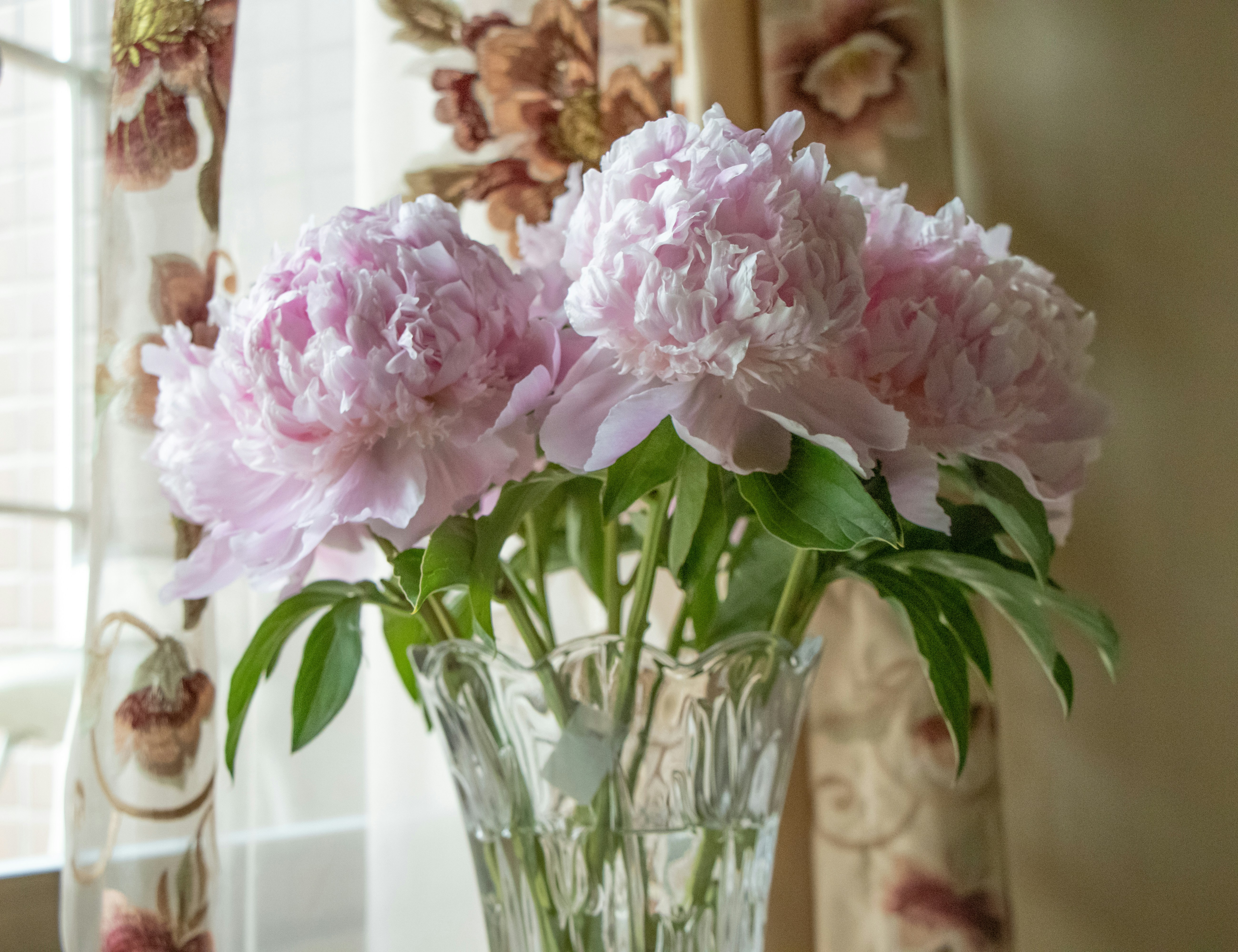 Dreamy pastel arrangement of soft roses and peonies in a clear glass vase