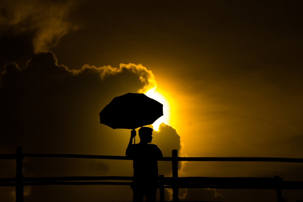 une personne tenant un parapluie devant le soleil