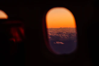 A vibrant sunrise view from an airplane window showing fluffy clouds below and a golden horizon.