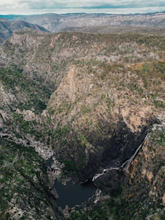 A panoramic view of a serene waterhole surrounded by rugged cliffs and sparse vegetation.