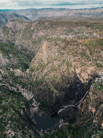 A panoramic view of a serene waterhole surrounded by rugged cliffs and sparse vegetation.