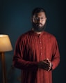 a man with a beard and glasses standing in front of a lamp