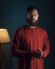 a man with a beard and glasses standing in front of a lamp