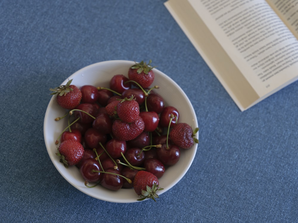 a bowl of cherries on a table next to a book