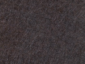 A close-up texture of a dark surface, possibly felt or wool, characterized by intersecting fibers and a soft, fibrous appearance.
