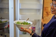 Smiling woman enjoying a fresh green salad in a sunlit kitchen.