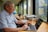 A middle-aged man sitting thoughtfully at a desk with a laptop and a cup of coffee.