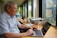 A middle-aged man sitting thoughtfully at a desk with a laptop and a cup of coffee.
