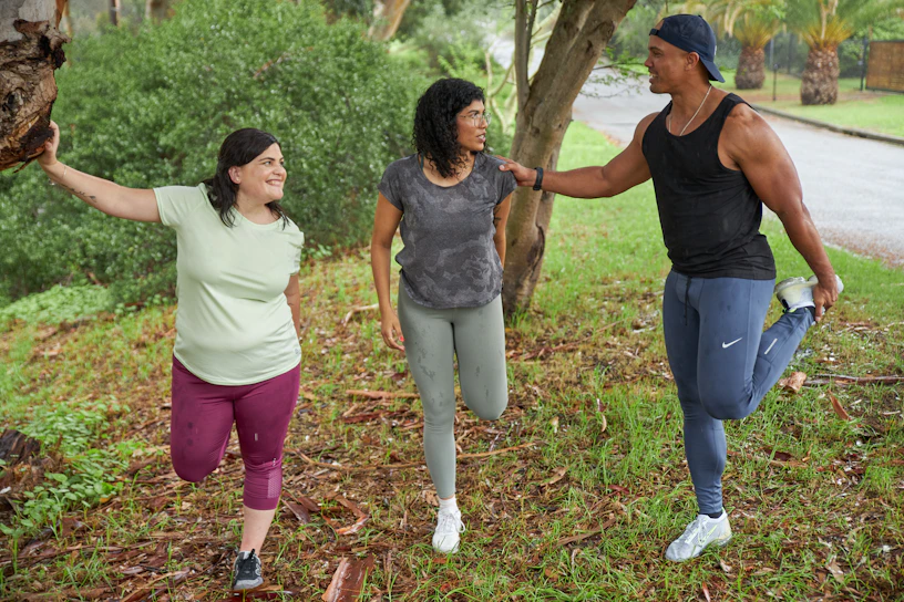 A group of teenagers stretching together outdoors in a sunny park, smiling and preparing for a fitness session.