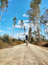 Cyclists riding along a dirt trail surrounded by open fields and blue skies.