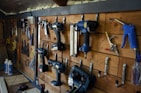 A well-organized workshop scene displays various power tools and hand tools neatly hung on a wooden wall. The tools include drills, screwdrivers, pliers, and wrenches, among others. The background is made of wooden planks, creating a rustic ambiance.