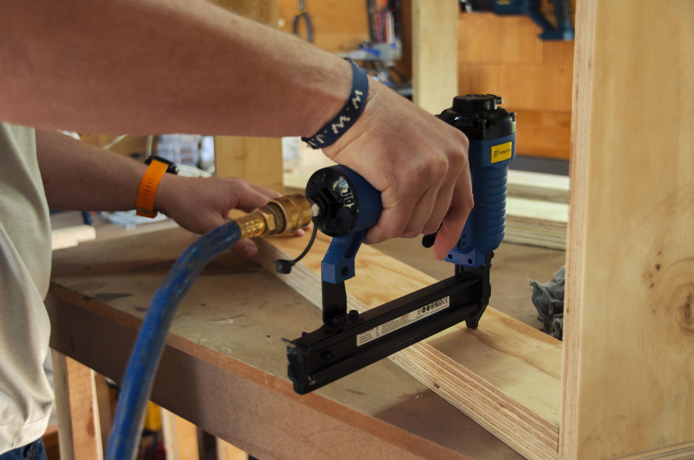 Craftsperson fastening a wooden frame with a pneumatic tool in a working workshop