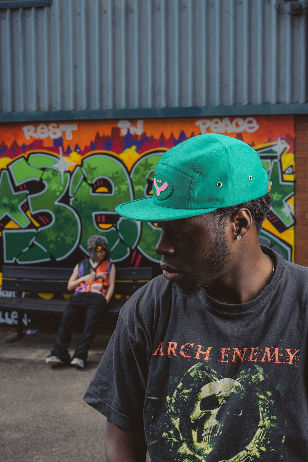 a man wearing a green hat standing in front of a graffiti covered wall