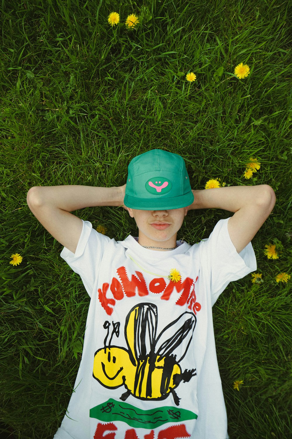 a boy laying in the grass wearing a green hat