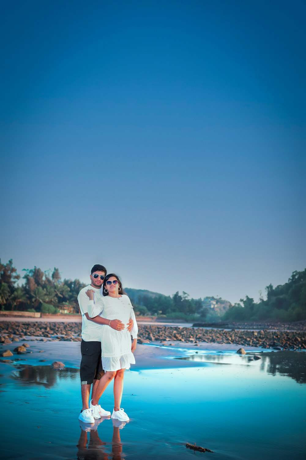 a man and woman standing on a beach next to a body of water